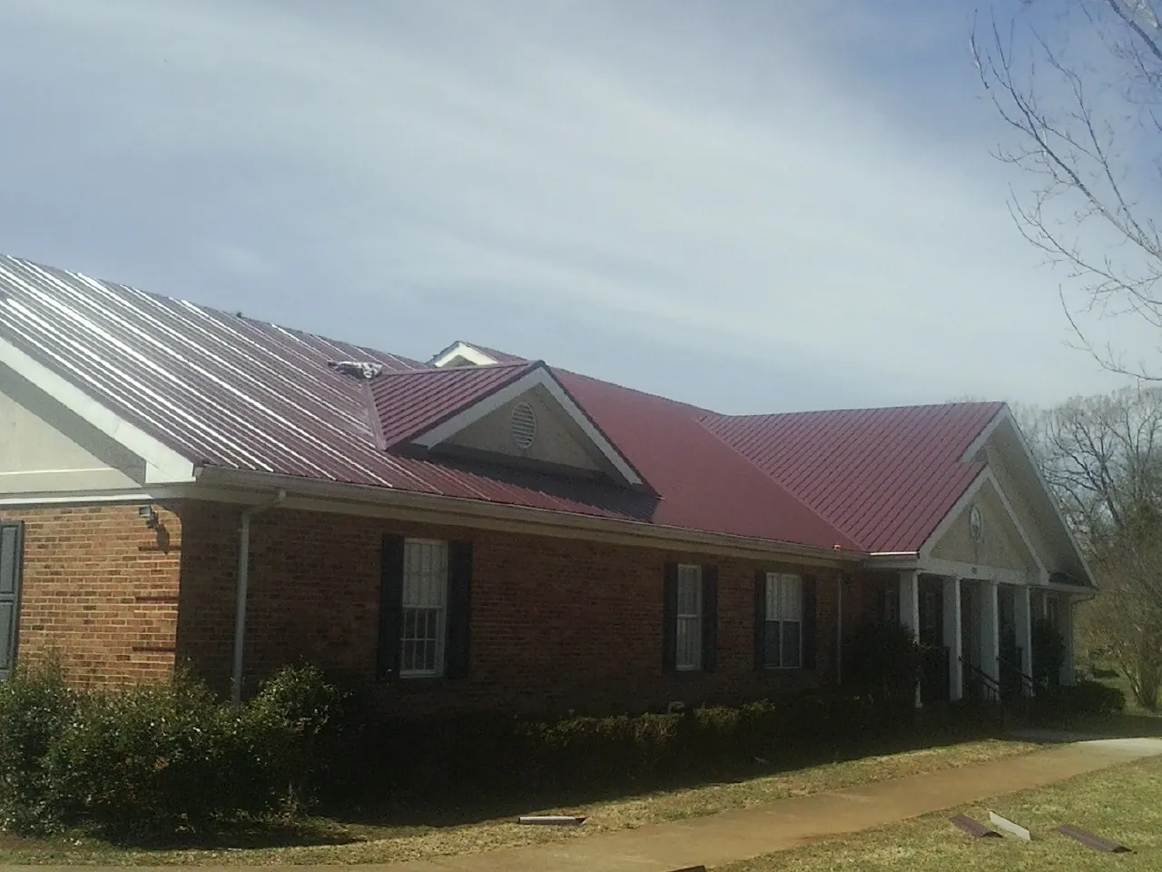 Red metal roof with gabled entries on a long brick building, from a Hail Damage Roof Repair job in Moapa